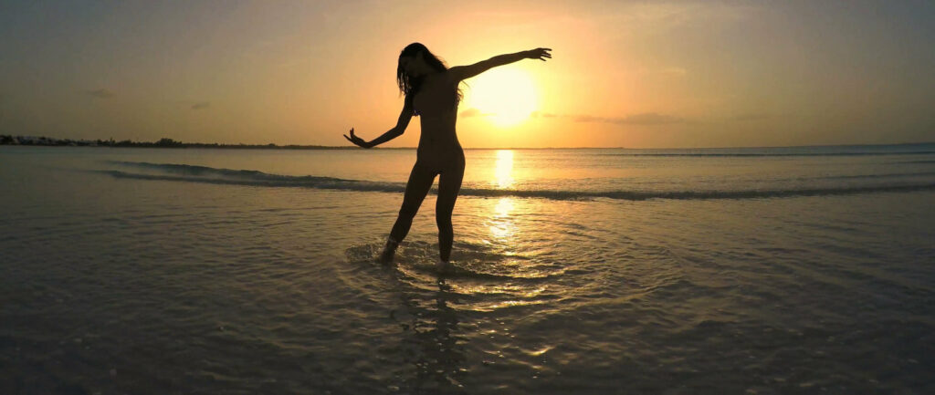 Frau tanzt im Sonnenuntergang an einem seichten Strand am Meer