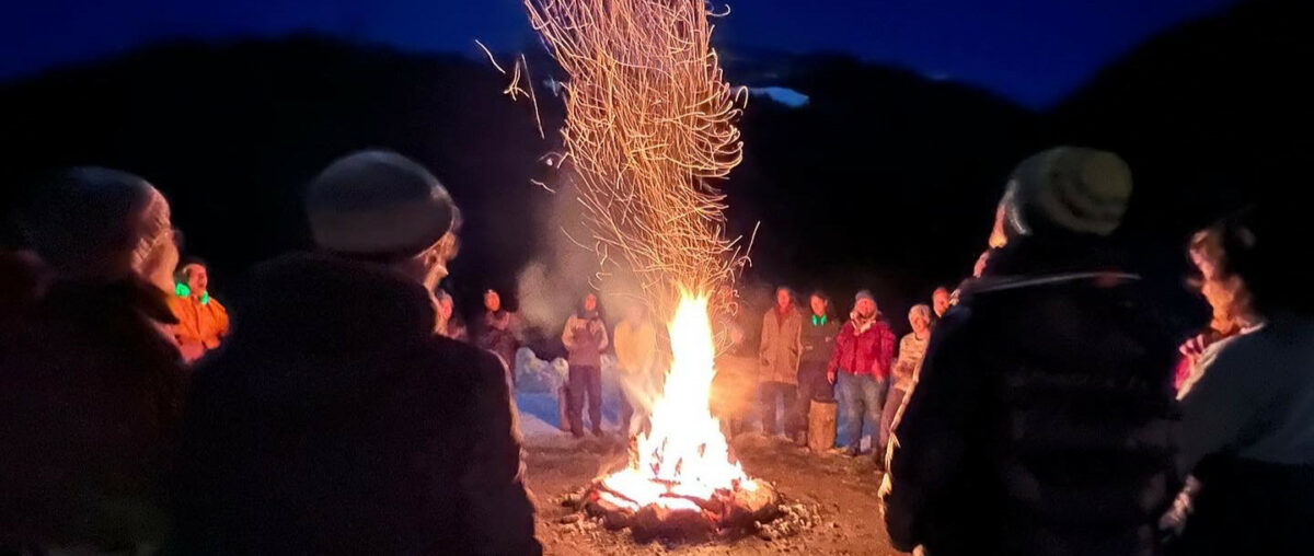 Gruppe steht nächtlicher Winterberglandschaft um ein Feuer