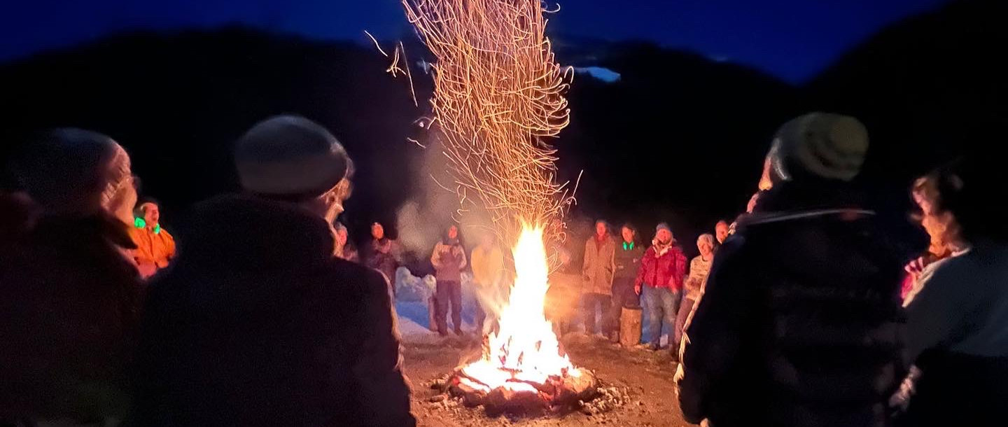 Gruppe steht nächtlicher Winterberglandschaft um ein Feuer